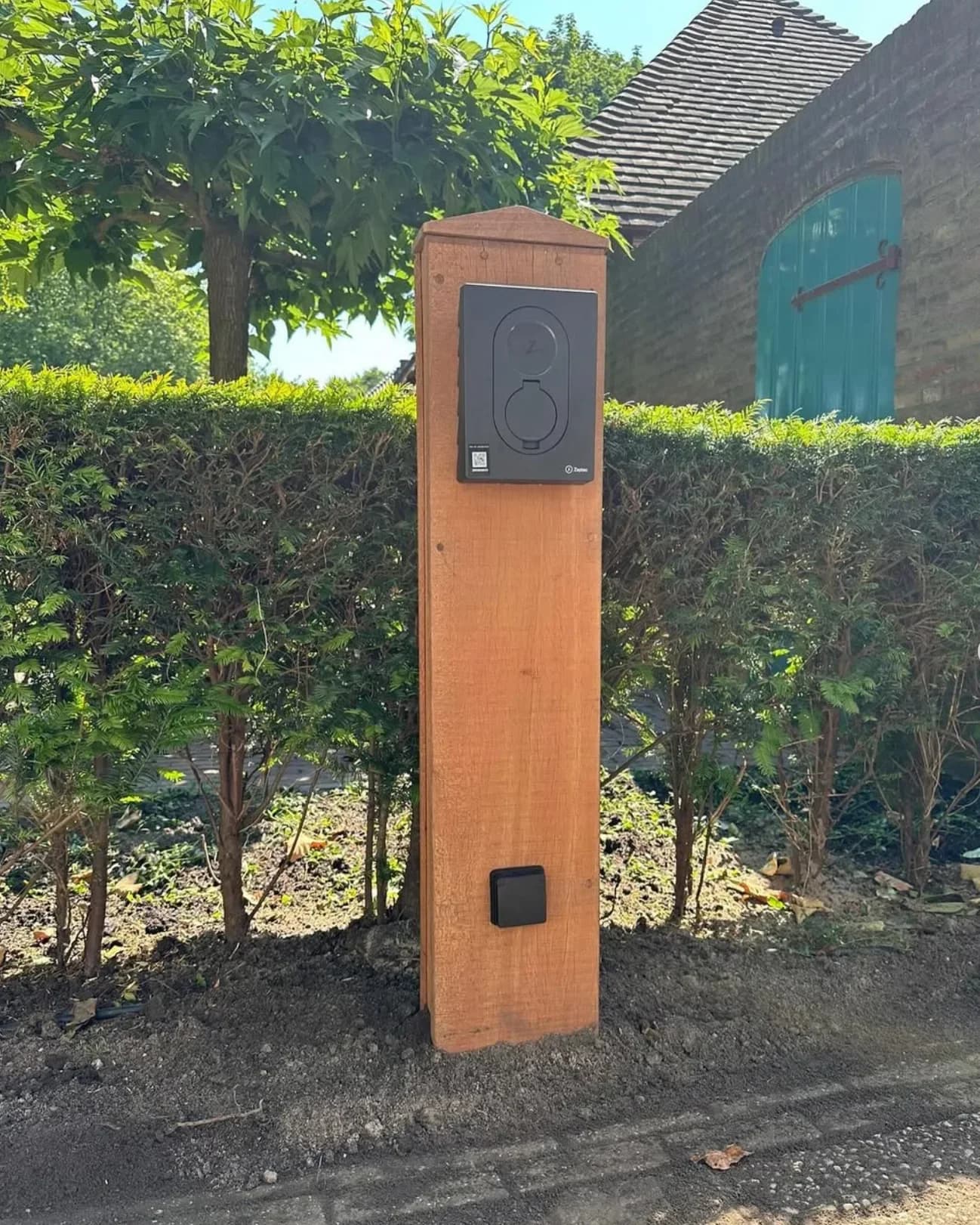 Zaptec-laadstation door HE Duurzaam gemonteerd op een houten paal in een tuin
